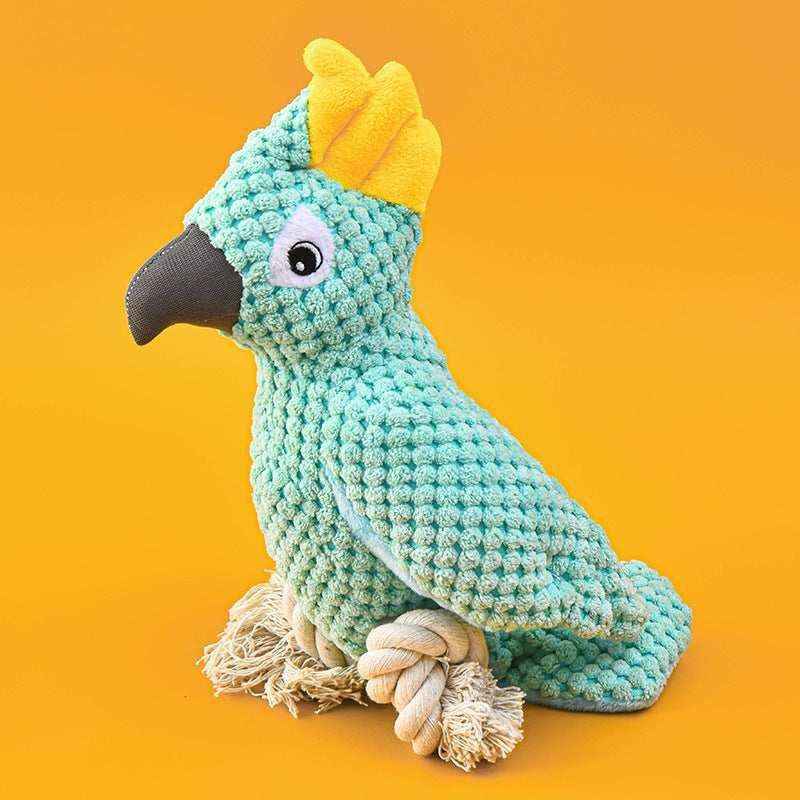 Plush parrot toy with textured turquoise body, yellow crest, black beak, and rope feet on orange background