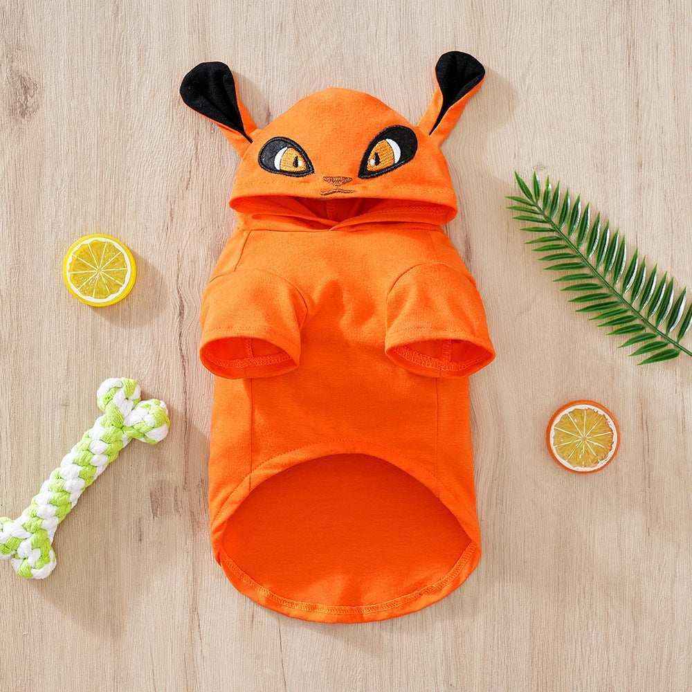 Orange pet hoodie with cartoon eyes and ears on wooden background with toy bone and green leaf