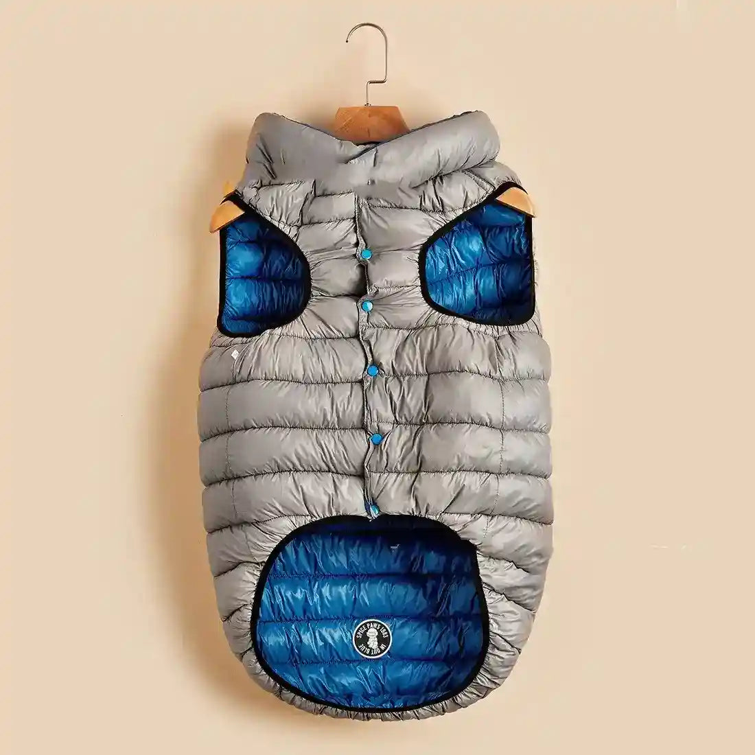 Gray and blue padded dog vest jacket with buttons, hanging on wooden hanger