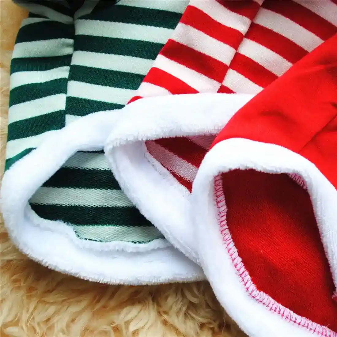 Close-up of red and green striped Christmas stockings with white fuzzy cuffs on a beige fur surface
