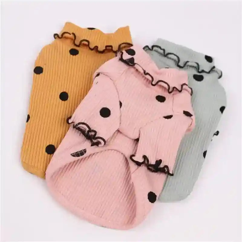 Three ribbed pet sweaters in pink, mustard, and gray with black polka dots and ruffled edges
