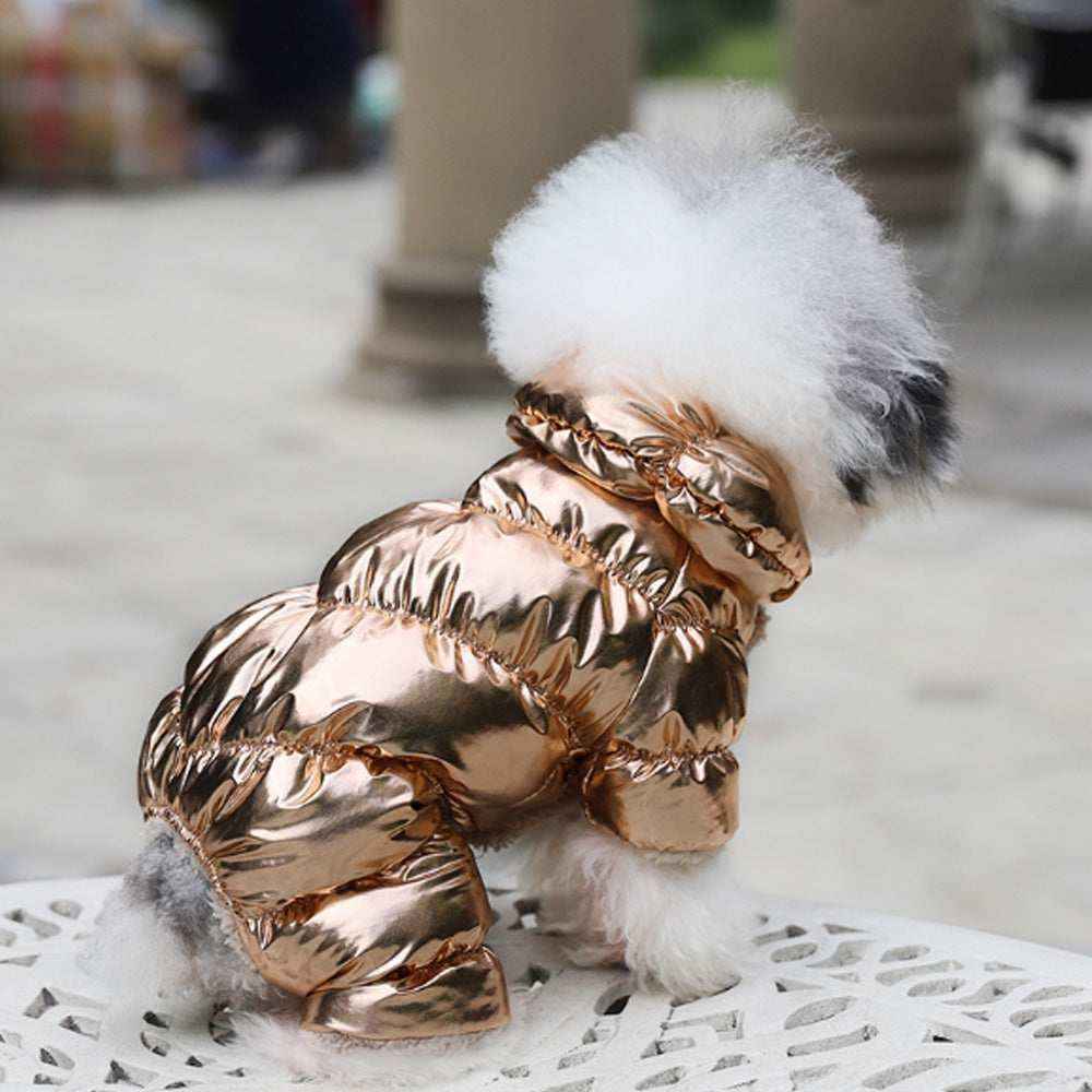Small fluffy dog wearing shiny metallic rose gold puffer jacket sitting on white ornate metal table