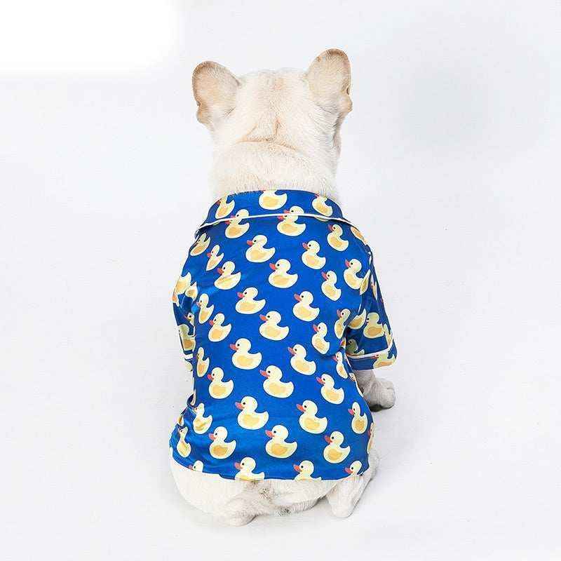 White dog wearing blue shirt with yellow rubber duck pattern sitting facing away on white background