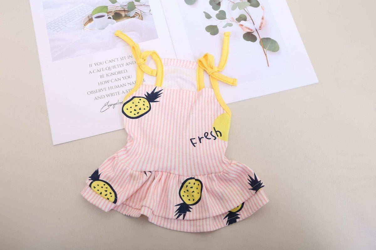 Pink striped baby dress with yellow pineapple print and tied shoulder straps on beige background
