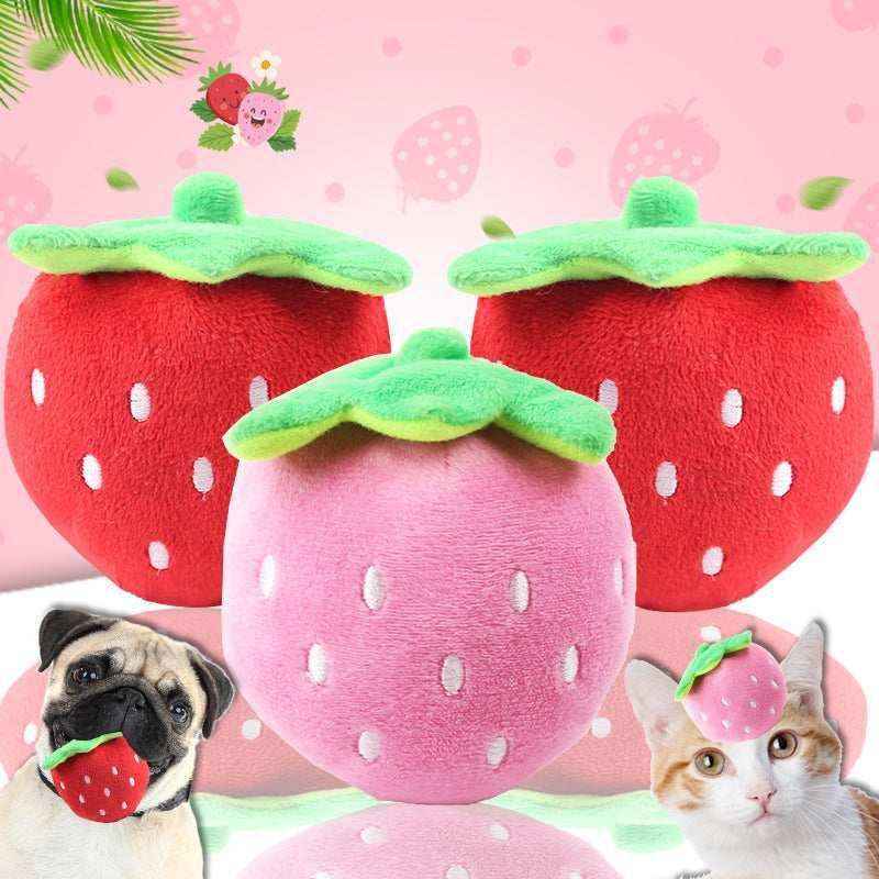 Plush red and pink strawberry pet toys with green leaves, a pug holding a strawberry toy and a cat wearing a strawberry hat