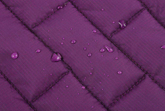 Close-up of water droplets on purple quilted waterproof fabric with detailed stitching