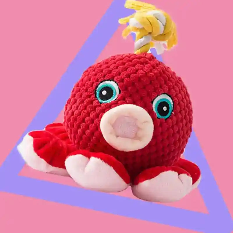 Red plush octopus toy with blue eyes and pink mouth on pink background with purple triangle