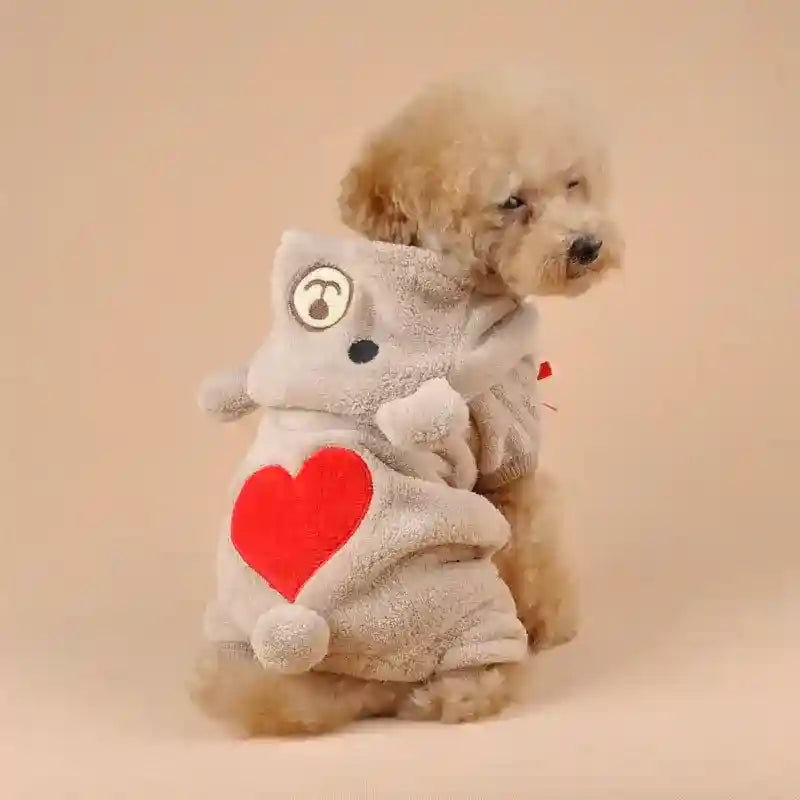 Small poodle dog wearing beige plush hoodie with red heart and bear face design on back