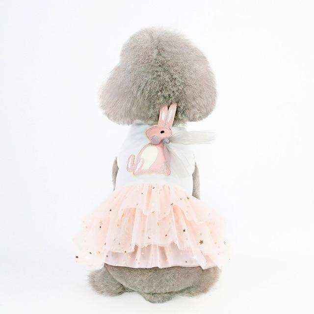 Gray poodle wearing white dress with pink bunny and layered tulle skirt with gold stars