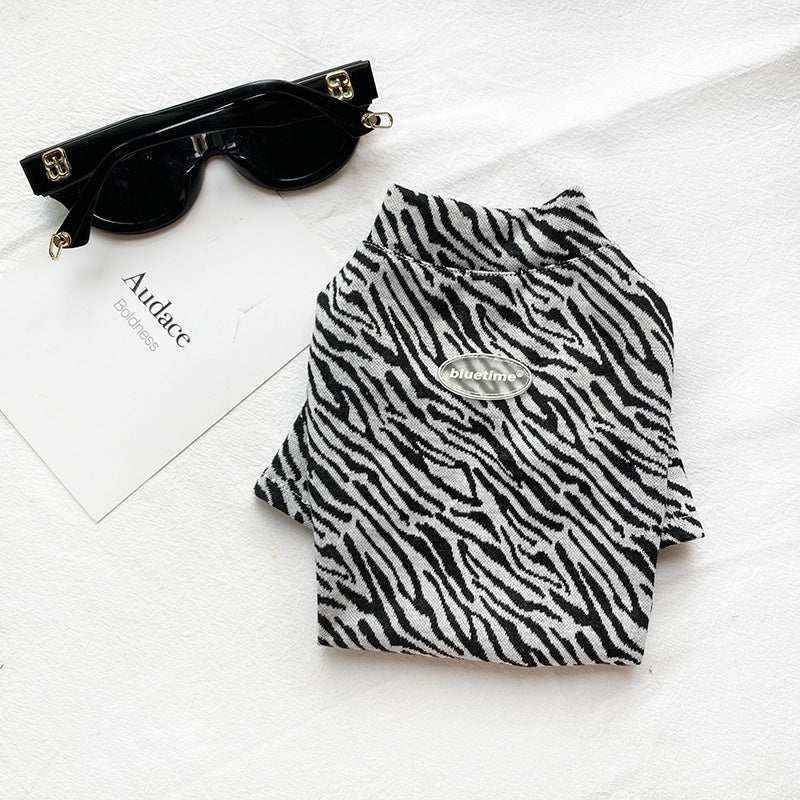 Black and white zebra print dog sweater with Bluetime logo next to black sunglasses on white surface