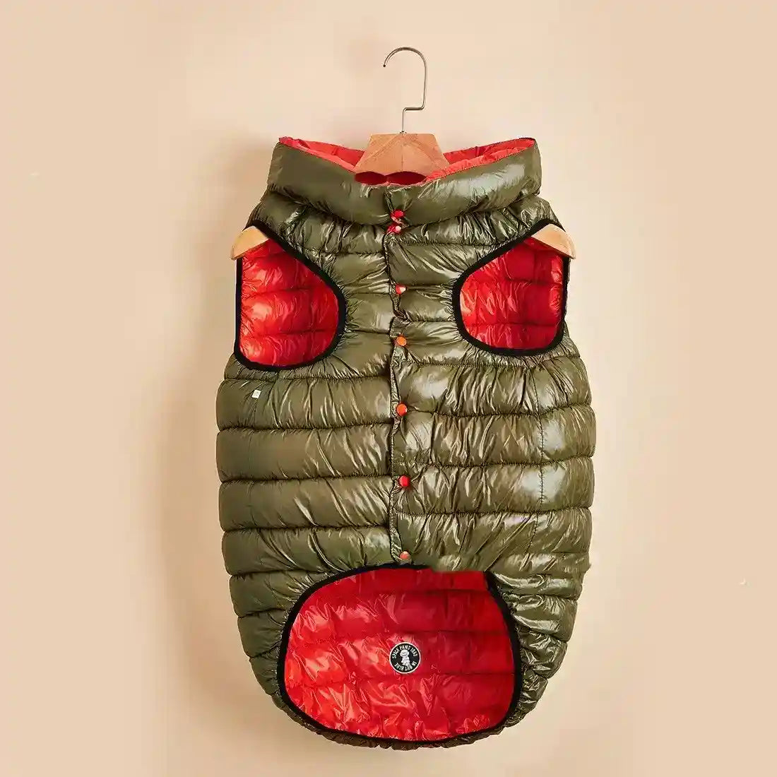 Olive green and red padded dog jacket with hood and button closure on a wooden hanger