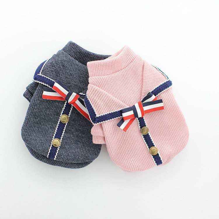 Two knitted dog sweaters in pink and gray with navy trim, gold buttons, and red-white-blue bows