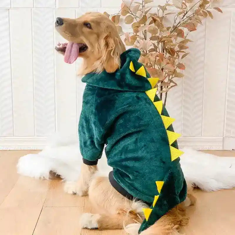 Golden retriever wearing green dinosaur hoodie with yellow spikes sitting indoors on wooden floor