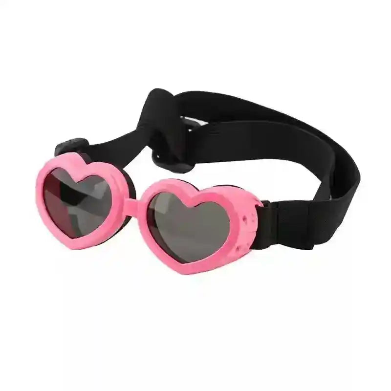 Pink heart-shaped goggles with dark lenses and adjustable black strap on white background