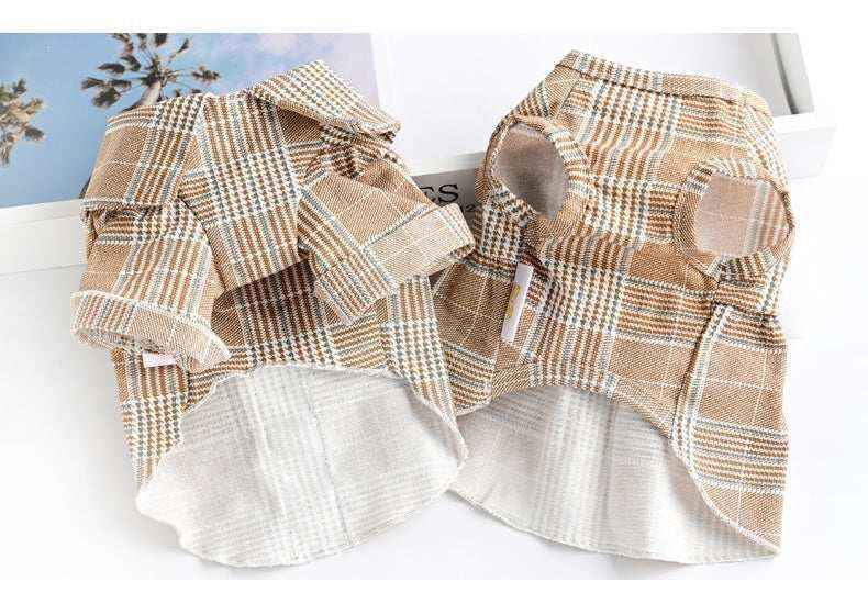 Two brown and white plaid dog shirts with collars and armholes laid on a white surface