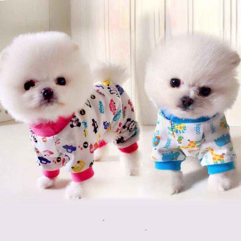 Two small white fluffy dogs wearing colorful animal and cartoon print pajamas indoors