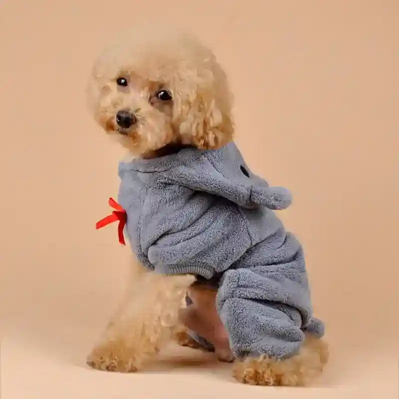Small curly-haired dog wearing a gray fleece onesie with a red bow on beige background