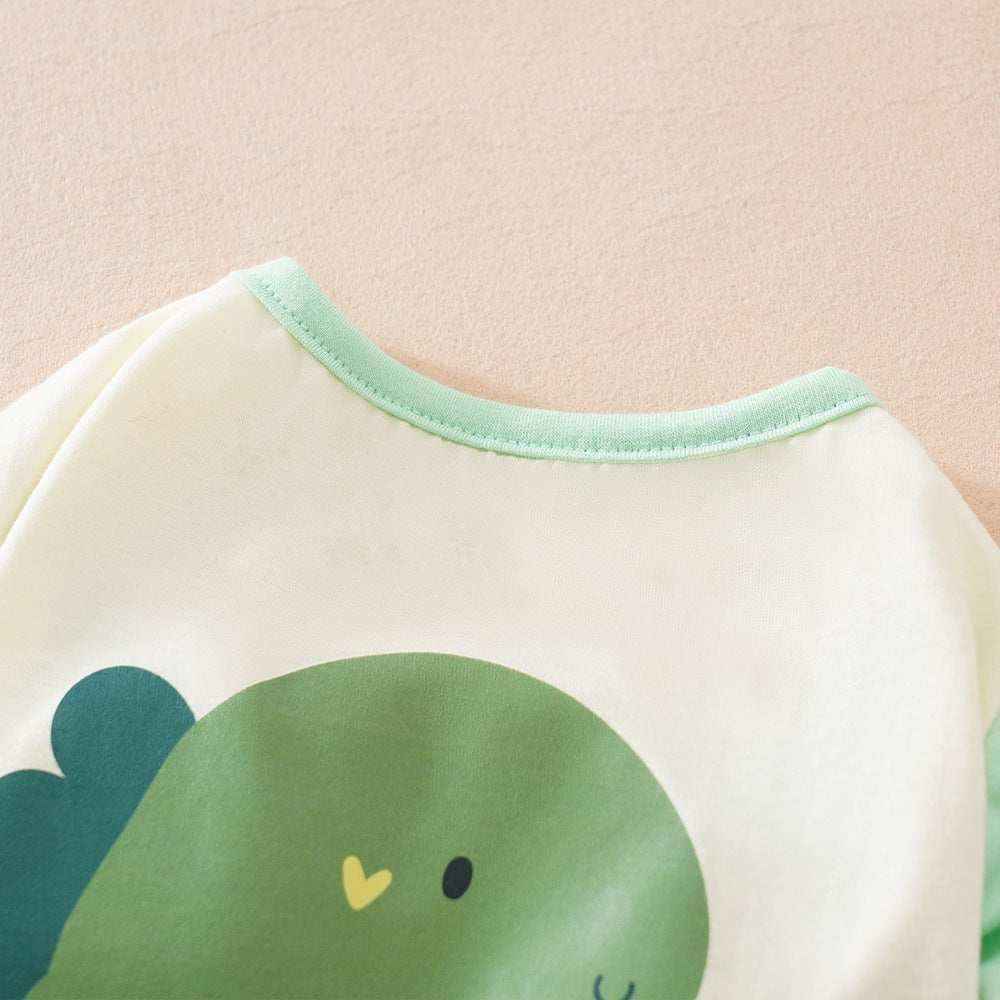 Close-up of green dinosaur print on white baby onesie with light green neckline and soft fabric