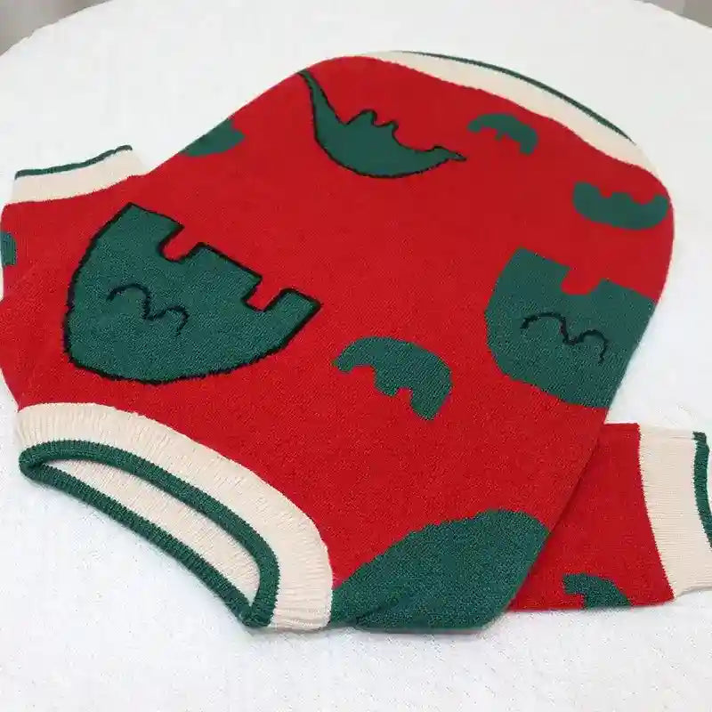 Red knit sweater with green castle and arch patterns, cream cuffs and collar, laid on white surface