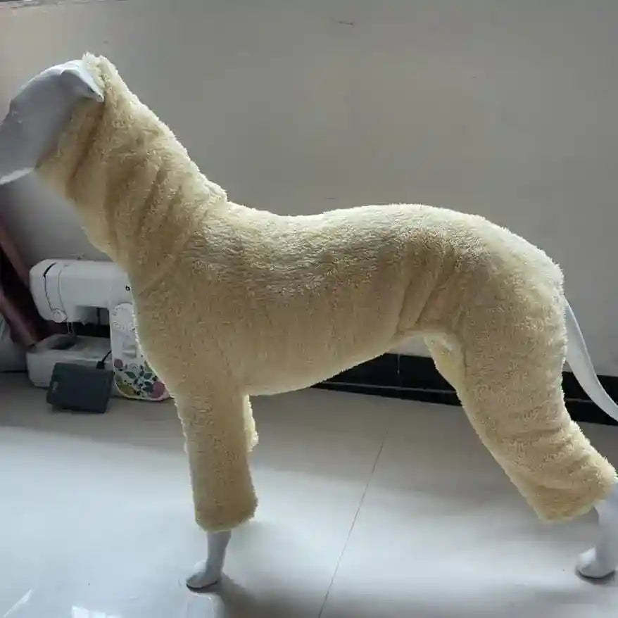 Cream-colored fleece dog jumpsuit displayed on mannequin in indoor setting with sewing machine nearby