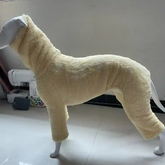 Cream-colored fleece dog jumpsuit displayed on mannequin in indoor setting with sewing machine nearby