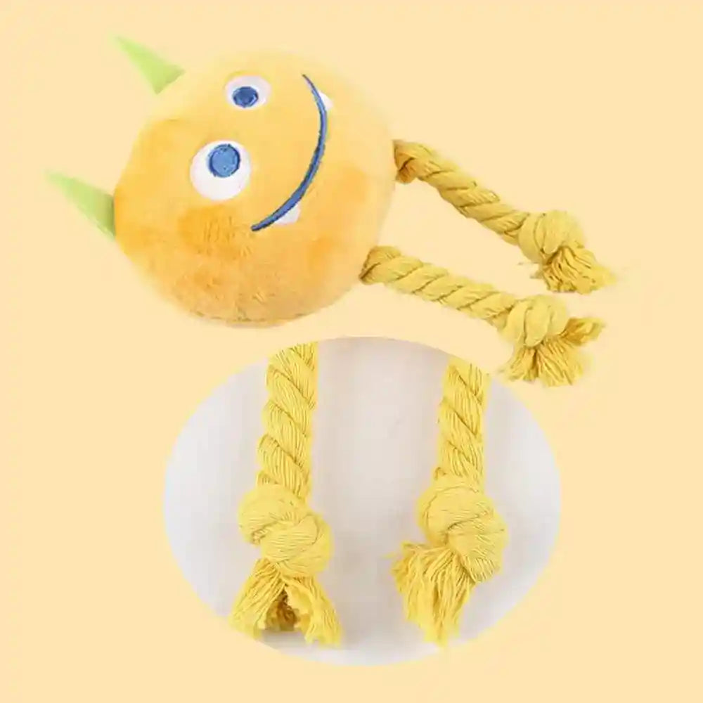 Yellow plush dog toy with smiling face, blue eyes, green horns, and knotted rope legs on yellow background