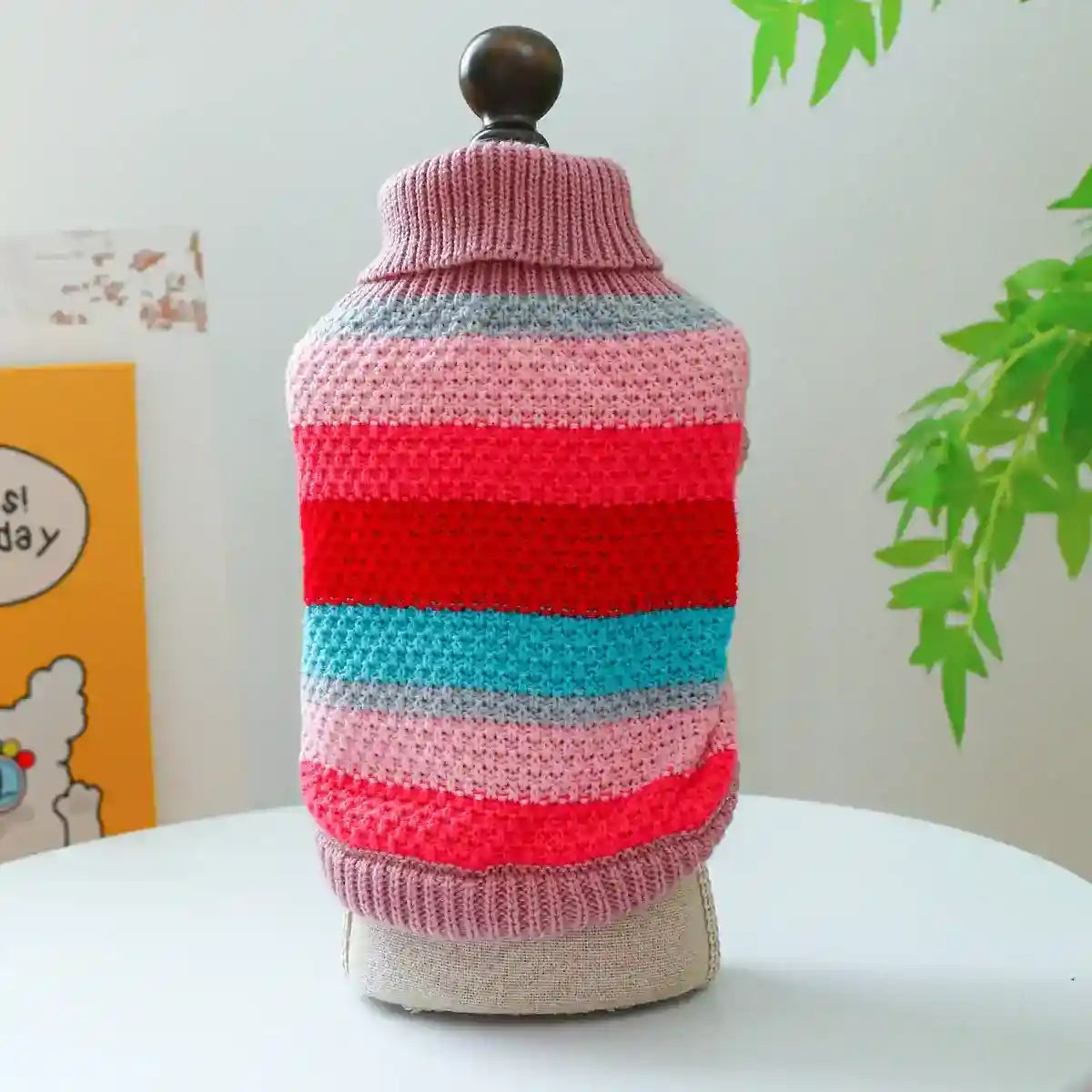 Colorful striped knit dog sweater on mannequin with green plant and cartoon wall art background