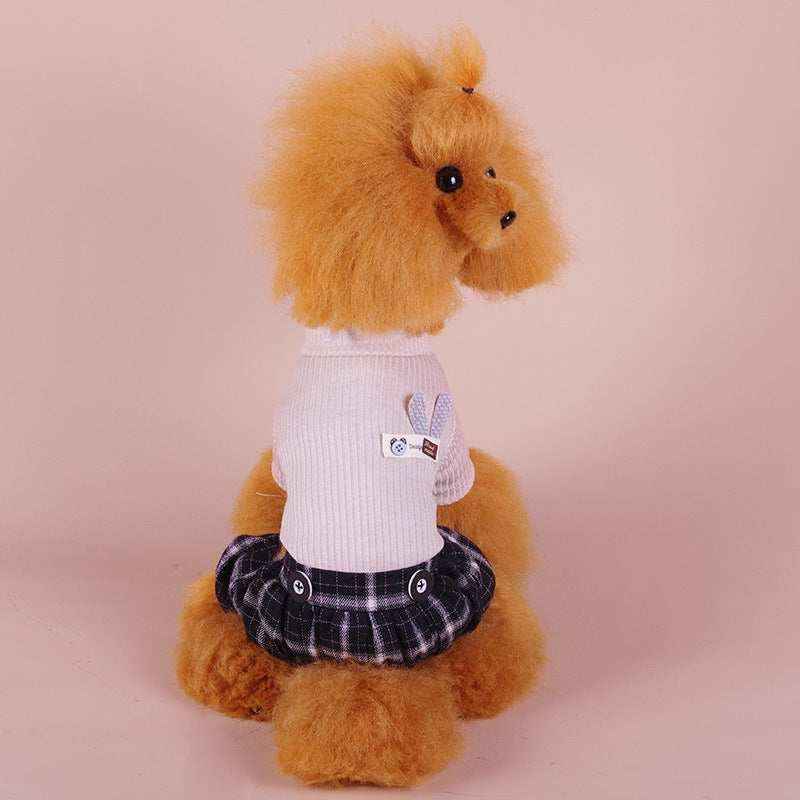 Fluffy brown poodle wearing a white sweater with a bunny patch and a black plaid skirt on a pink background