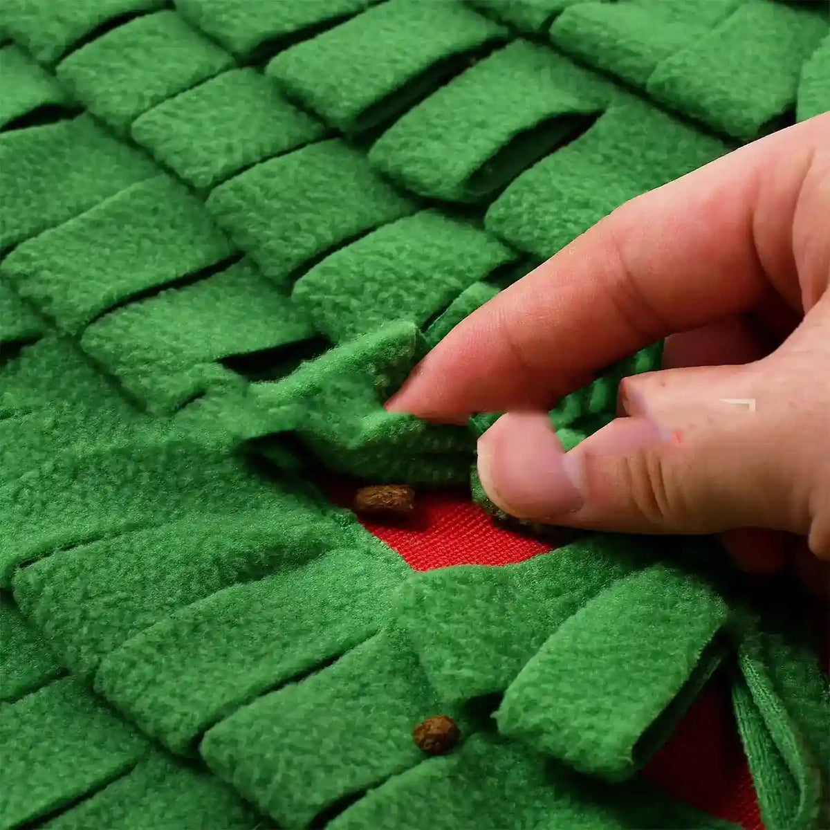 Hand lifting green fabric flap on red snuffle mat with hidden dog treats