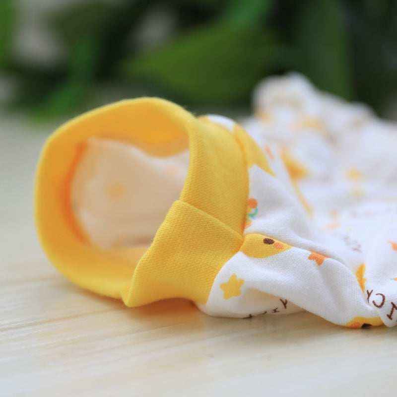 Close-up of a white baby romper with yellow cuff and duck print on a wooden surface