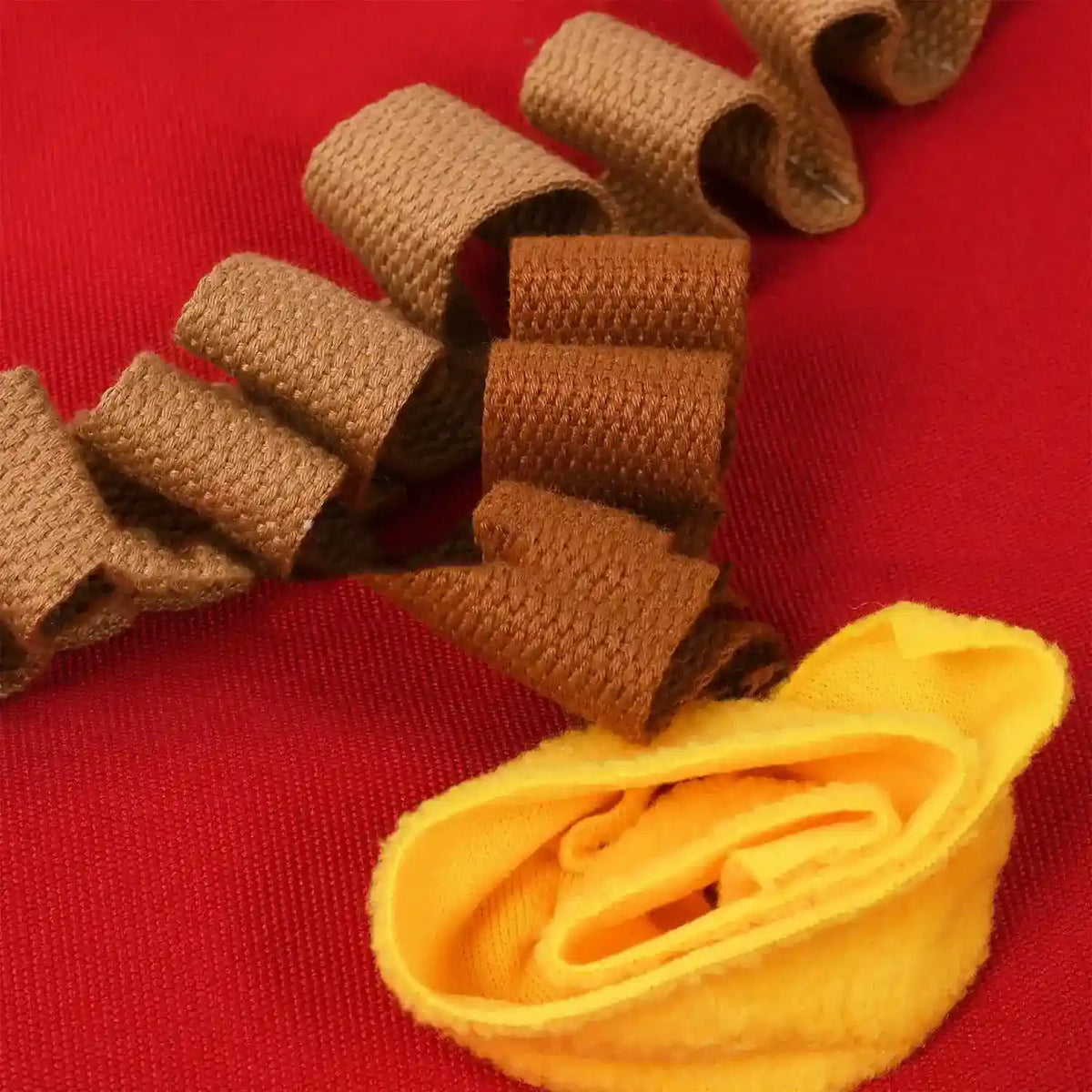 Curled brown and yellow fabric ribbons on textured red background, showcasing textile details