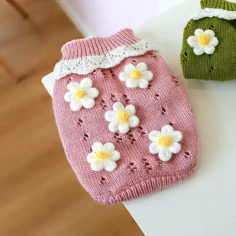 Pink knitted dog sweater with white and yellow daisy decorations and ruffled collar on a white table