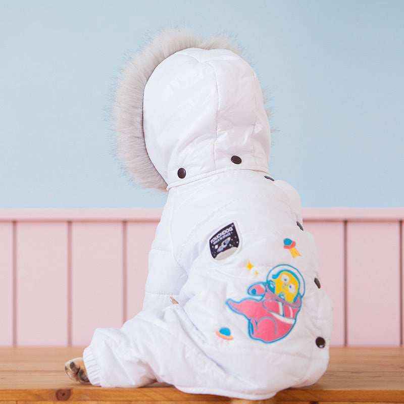 Small dog wearing white winter coat with fur hood and space-themed patch sitting on wooden surface