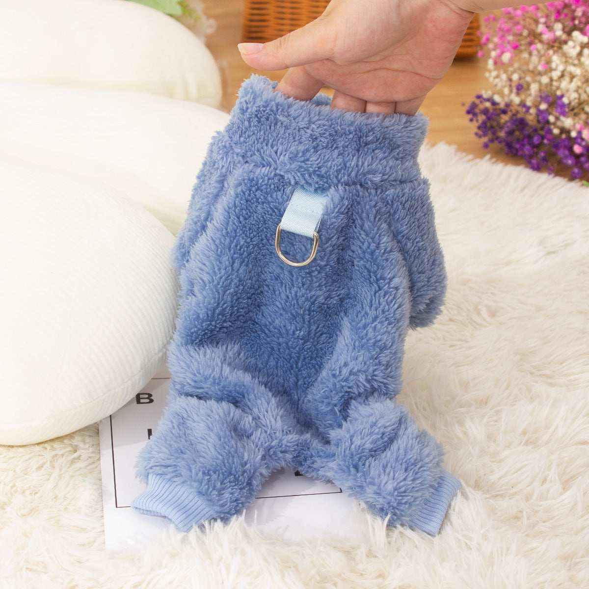 Hand holding a soft blue plush dog sweater with a collar loop on a white furry rug
