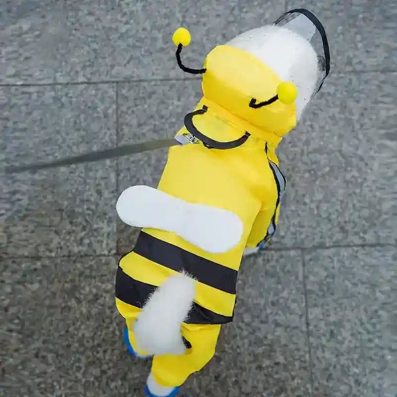 Small white dog wearing yellow bee costume with black stripes and face shield walking on stone pavement