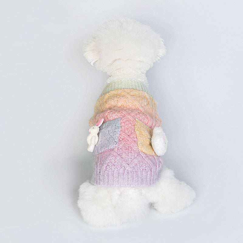 White fluffy dog wearing a pastel multicolor knitted sweater with bunny decorations