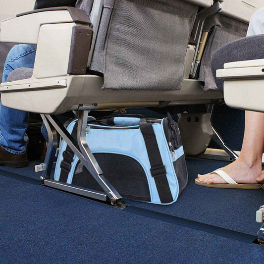 Light blue soft pet carrier bag placed under airplane seats on blue carpet floor