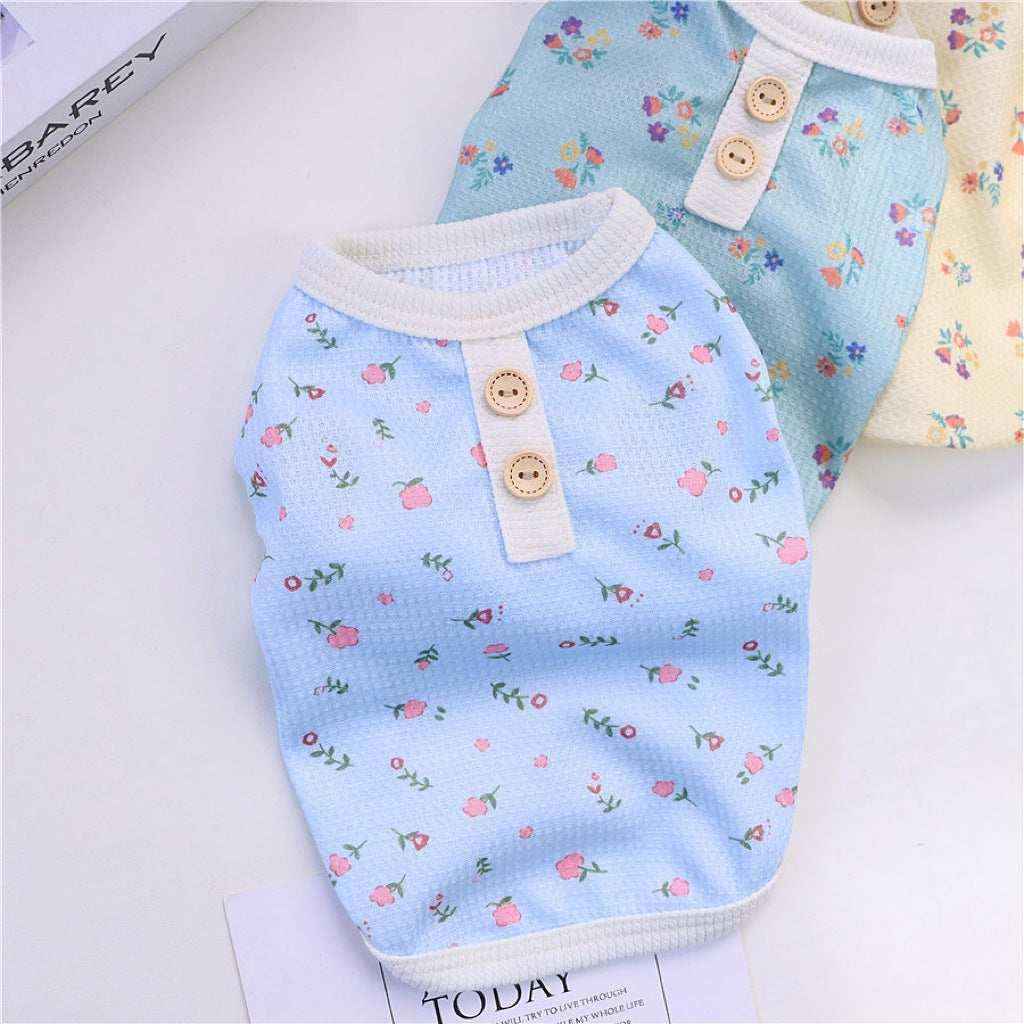 Small floral patterned pet clothes in blue, green, and cream with wooden buttons on a white surface