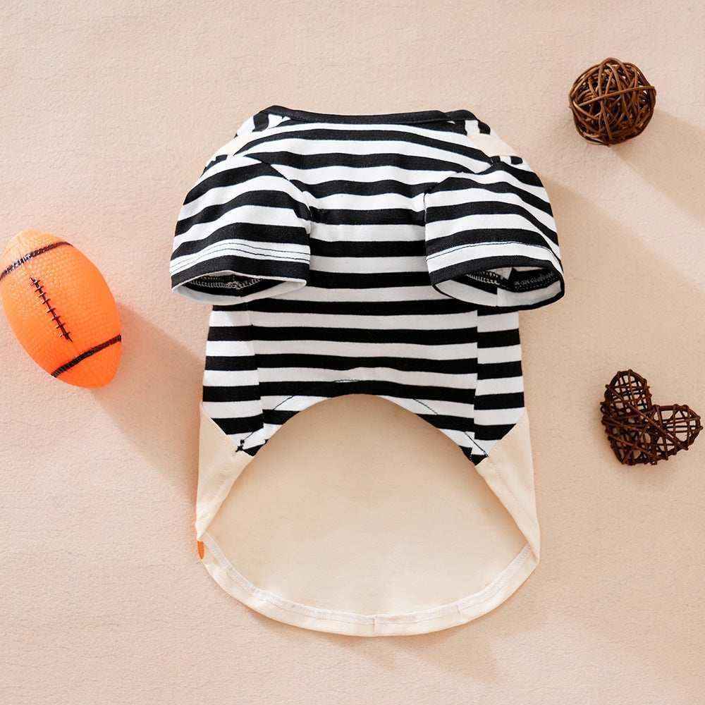 Black and white striped pet shirt with short sleeves on beige surface, orange toy ball and brown wicker decor