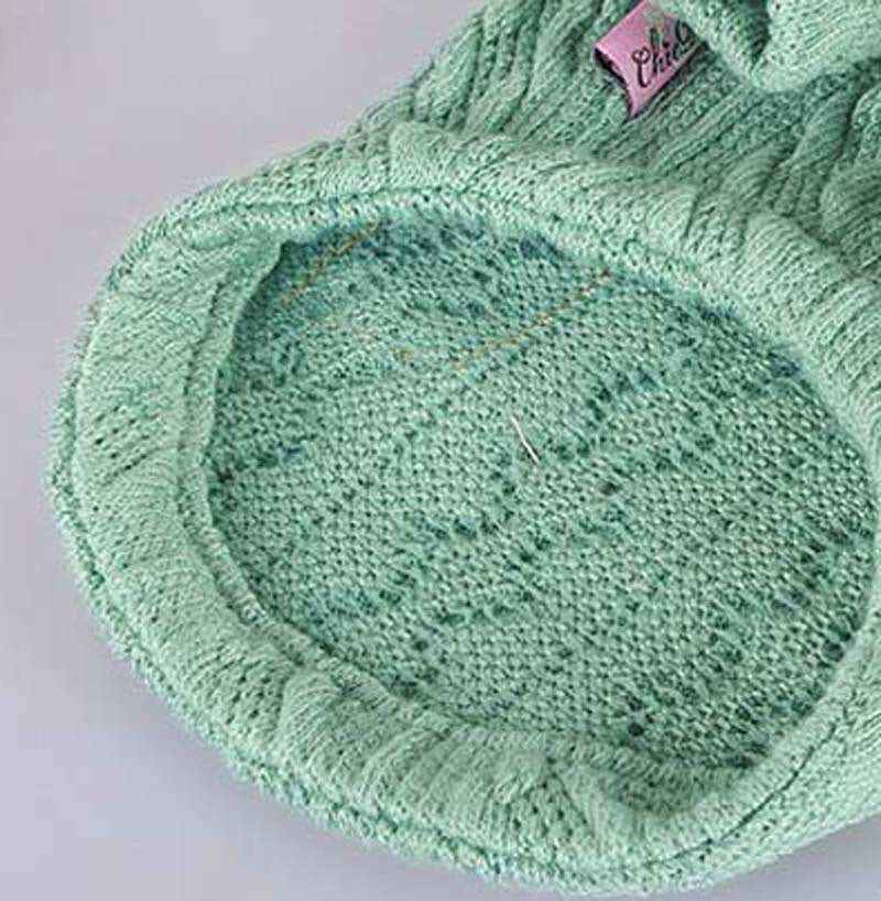 Close-up of a mint green knitted beanie hat with a pink label on a gray background