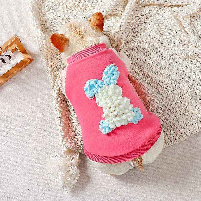 Small dog wearing pink sweater with 3D white and blue bunny design lying on cream knitted blanket