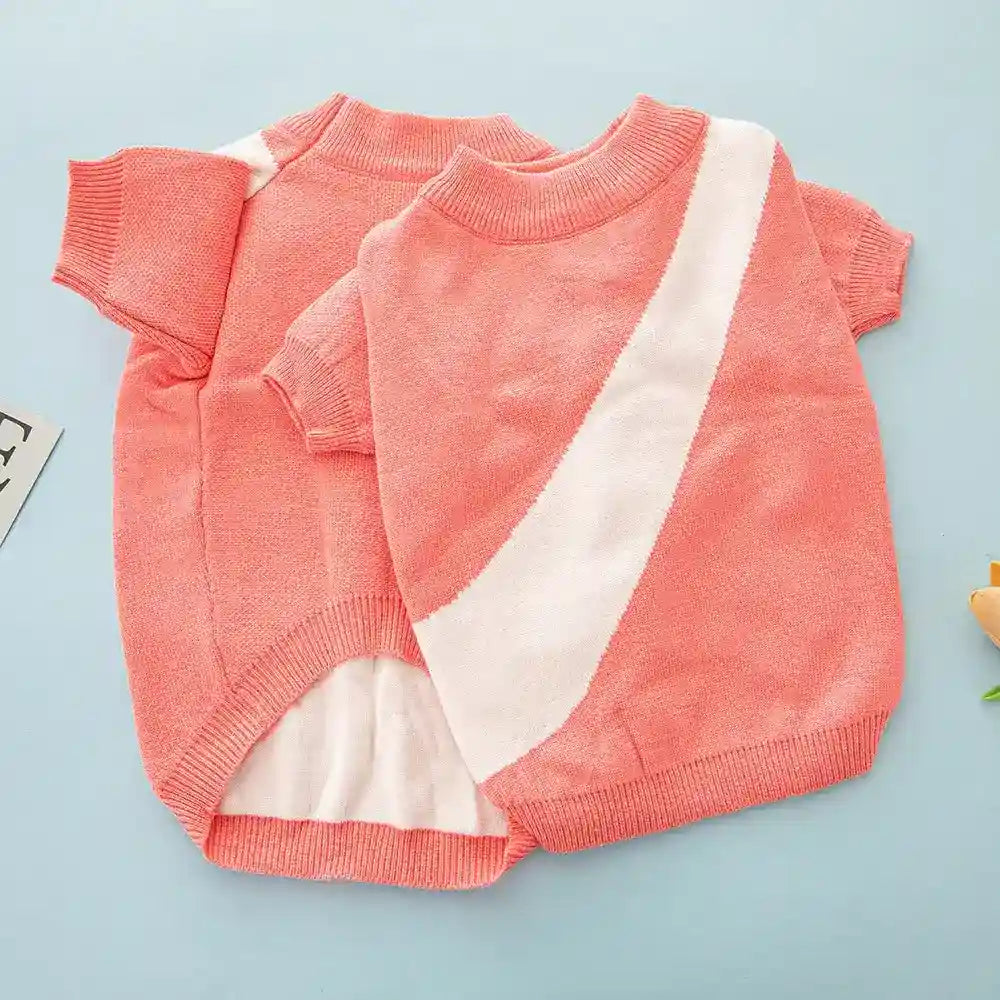 Two coral pink knitted pet sweaters with short sleeves and white diagonal stripe on blue background