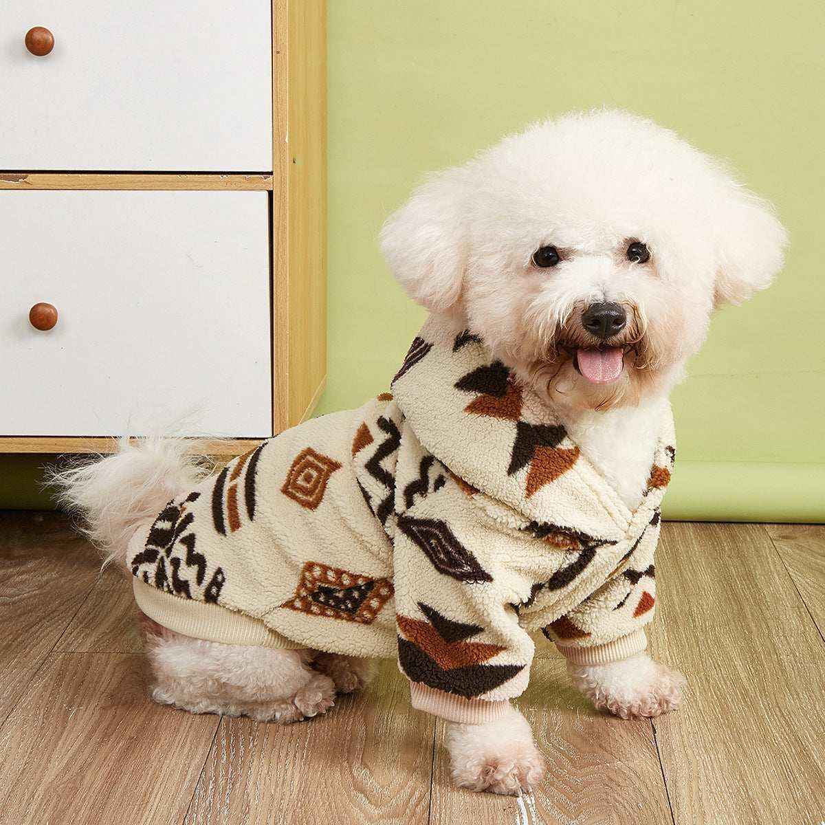 Small white fluffy dog wearing cozy patterned fleece hoodie standing on wooden floor