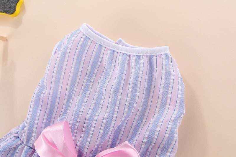 Close-up of striped pink and blue pet dress with white trim and pink satin bow on beige background