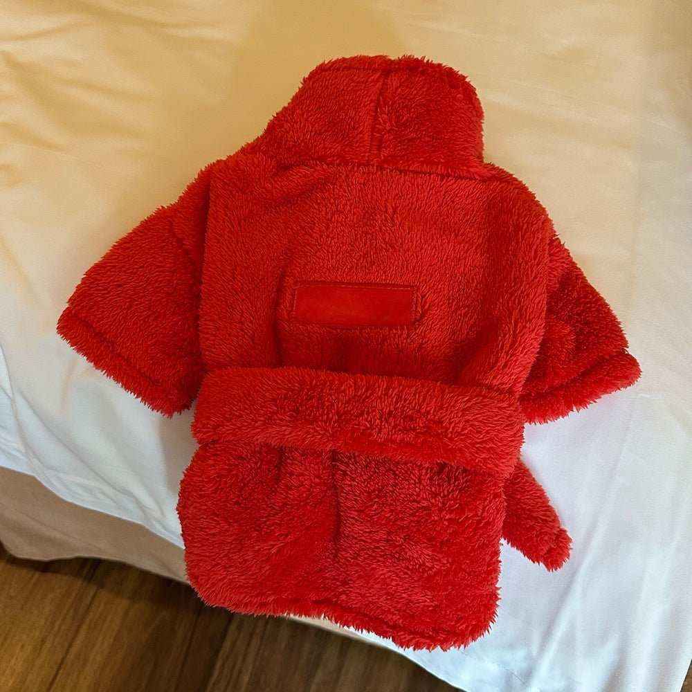 Red fluffy absorbent dog bathrobe with short sleeves laid on white bed cover