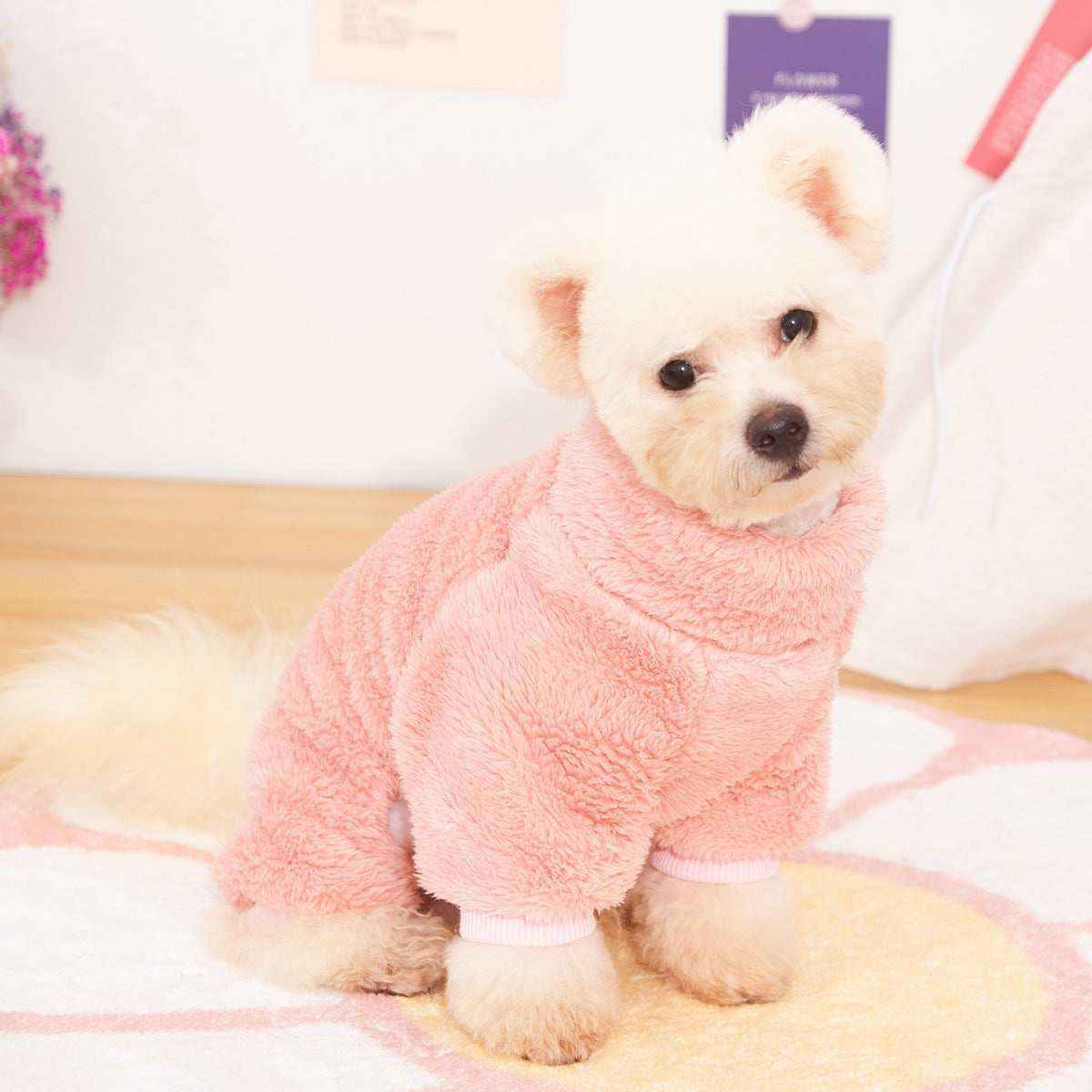 Small fluffy white dog wearing a soft pink fuzzy sweater sitting indoors on a patterned rug