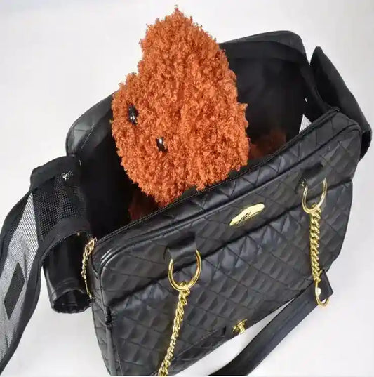 Black quilted eco-leather dog carrier bag with gold chains and small brown curly-haired dog inside