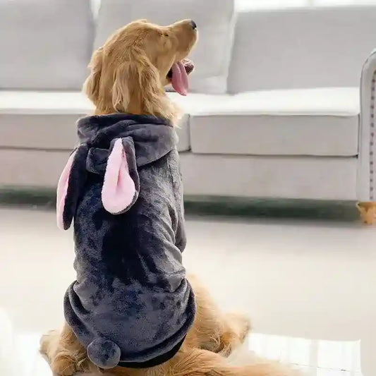 Golden retriever wearing a gray plush hoodie with pink bunny ears and tail sitting on floor