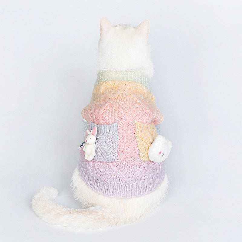 White cat wearing pastel multicolor knitted sweater with bunny and bear plush toys on pockets