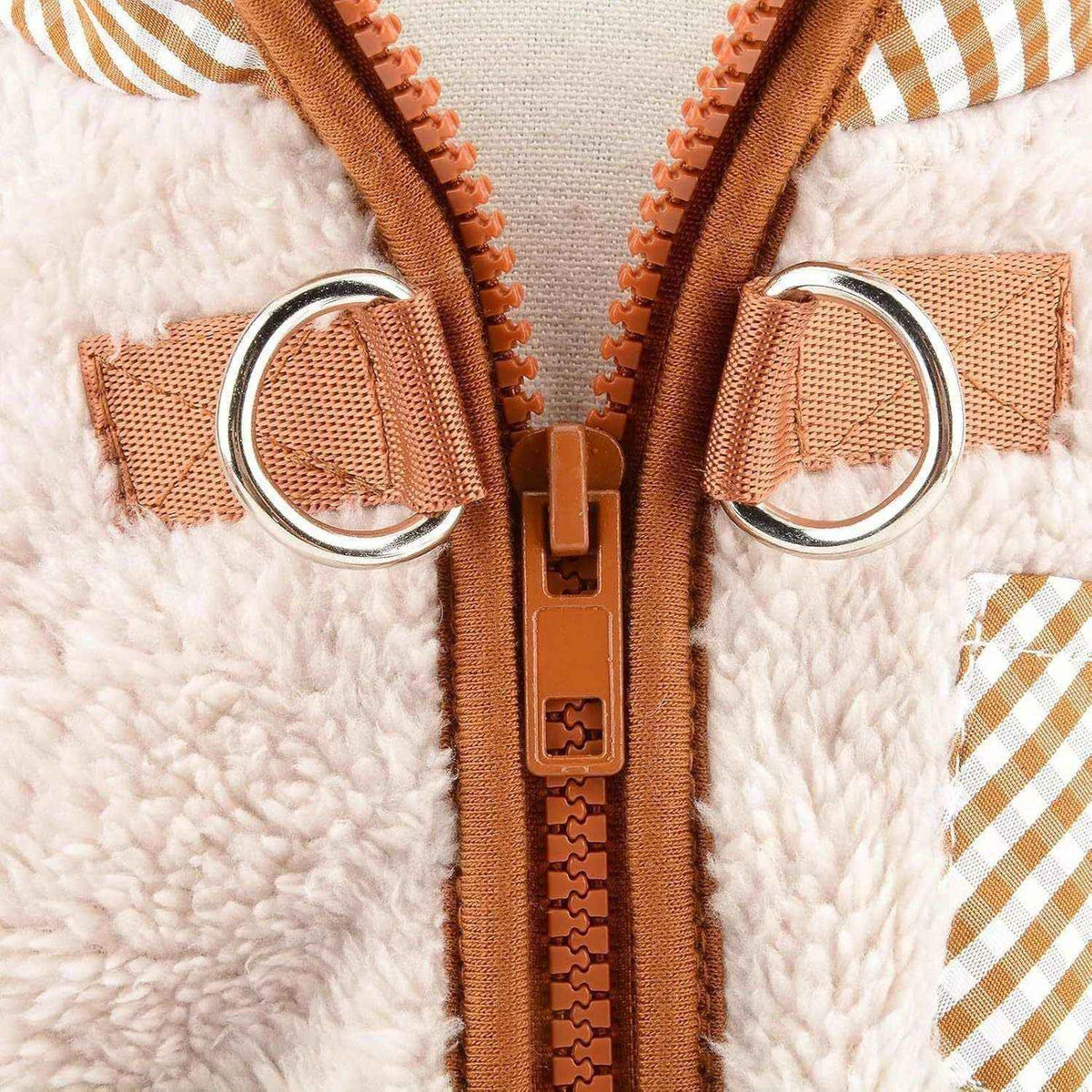 Close-up of beige sherpa fleece jacket with orange zipper and silver metal D-rings detail